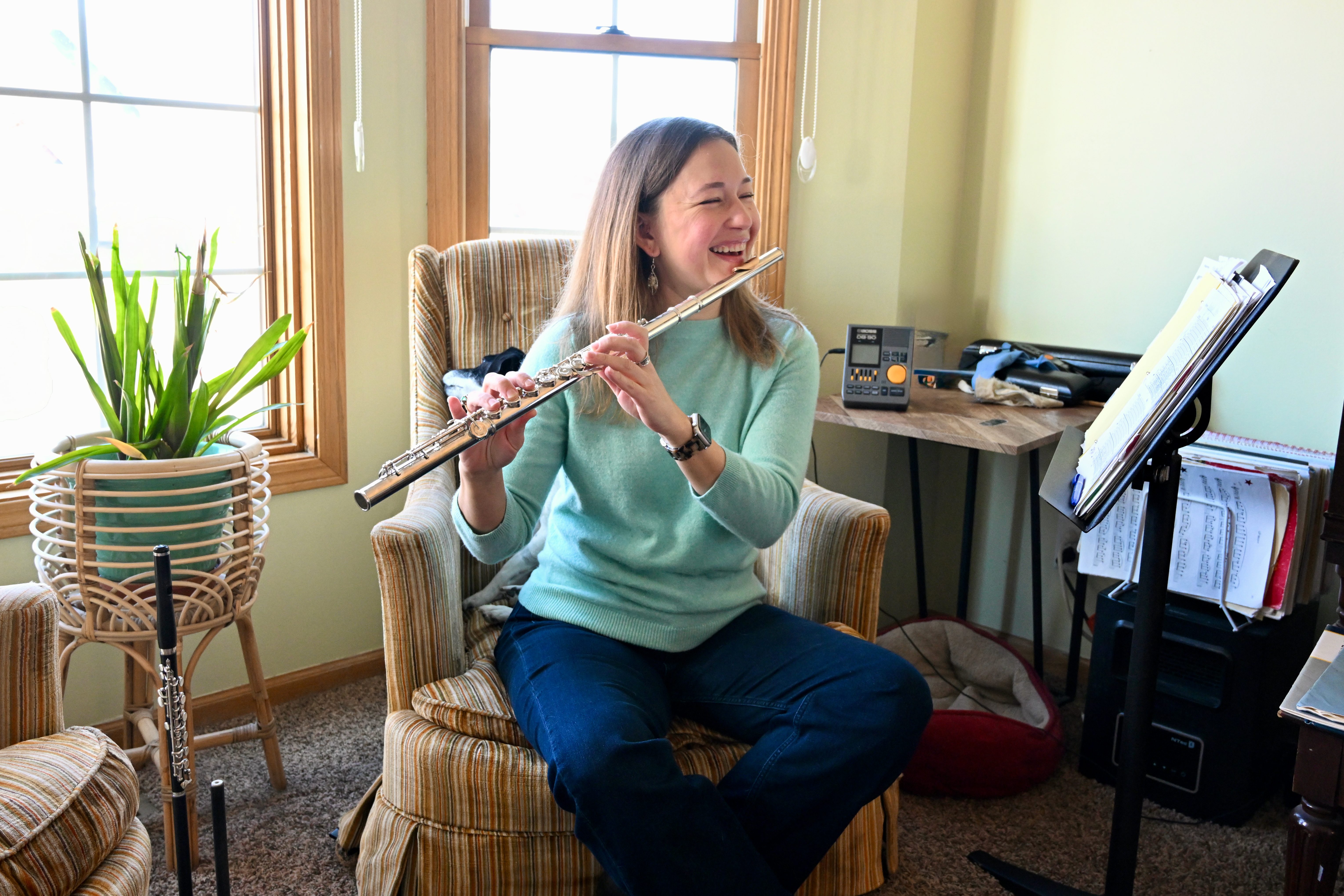 Lindsay in her home teaching space, holding her flute, surrounded by music, supplies, and a piccolo. Photo by AVDude.